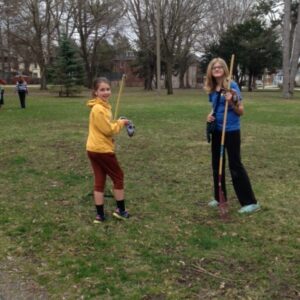 Two young girls with rakes smiling for a photo in a park with trees