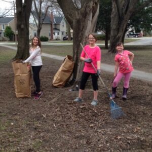 three young girls with bags and rake participating in cleanup at park