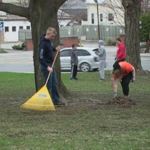 group of young kids cleaning up grassy area with street and houses in the background
