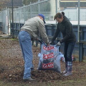 Man and woman filling ground debris in a bag near an outdoor hockey rink